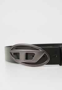 Black leather belt featuring a rounded metallic buckle with an oval shape and a cutout design, with multiple adjustment holes along the strap.