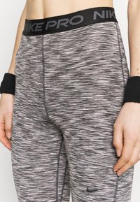 Nike Pro legíny v šedé a růžové barvě s texturovaným proužkovaným vzorem. Vybaveny širokým černým páskem s nápisem "NIKE PRO" a malým logem.