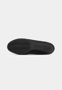 Semelle de chaussure noire avec un motif en vagues texturé pour une meilleure adhérence, dotée d'une section lisse près du talon et d'un logo vers l'arrière.