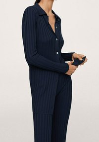 Conjunto de ropa de estar en azul marino, con relieve y de manga larga. La camisa cuenta con un cierre de botones y cuello. Los pantalones son ajustados y texturizados.