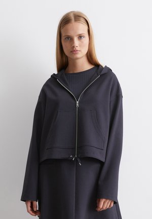 Cropped dark gray hoodie in soft fabric with a zip front, hood, and front pocket. Features a drawstring at the hem and wide sleeves.