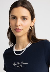 Tumes sinine särk heleda äärisega, millel on brodeeritud tekst; koos pärlkaelakee ja kuldsete rõngastuuridega kontrasti ja detaili loomiseks.