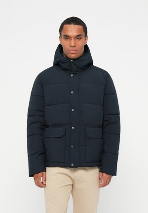 Marineblå pufferjakke med hætte, featuring en knaplukning, forlommer og et quiltet design for isolering og varme.