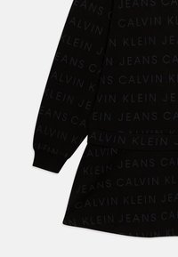 Crni dukserica s ponavljajućim uzorkom "Calvin Klein Jeans" u tamnosivoj boji. Rebrasti rukavi i donji rub, mekana tkanina.