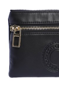 Bolsa de imitación de cuero negra con un cierre dorado y detalle de logo circular en relieve. Textura suave con una forma rectangular compacta.