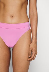 Rózsaszín bikini alsó, sima textúrával, magas derékkal és finom oldalsó kivágásokkal. Öltött részlet a derékon.