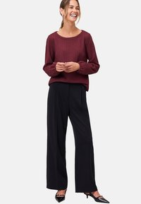 Pull en maille bordeaux avec un motif texturé, col rond, et pantalon noir à jambes larges, associé à des escarpins noirs à bout pointu.