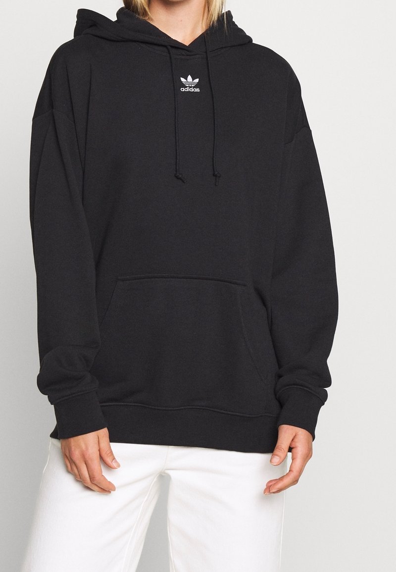 Černá mikina Adidas s velkou přední kapsou, kapucí na šňůrku a minimálním bílým logem na hrudi. Materiál směsi bavlny.