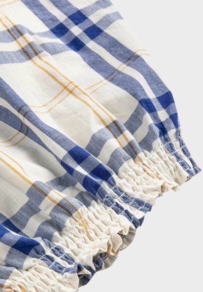 Gros plan sur un tissu à carreaux bleu, blanc et jaune avec un bord élastiqué et froncé sur la manche ou le poignet d'un vêtement.