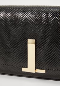 Mustekki musta nahkainen clutch, jossa on kultainen metallinen lukko. Ominaisuuksiin kuuluu matelijanahka-kuvio ja suorakulmainen koriste sulkemisessa.