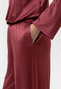 Bordeaux loungewear set met een losvallend bovenstuk met lange mouwen en broek met elastische taille en zijvakken, gemaakt van een gladde stof.