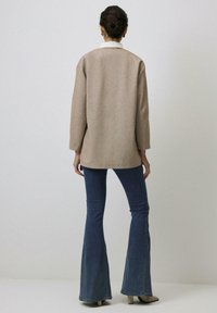 Beige wollen blend cardigan met een ruime pasvorm en een brede kraag, gecombineerd met flare denim jeans. De outfit heeft een minimalistisch ontwerp.