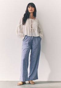 Valge tekstuuriga pluus ees lipsuga ja pitsdetailidega; sinised lahtised püksid peene mustriga; helepruunad punutud sandaalid.