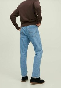 Lichtblauwe denim jeans met een recht model, voorzien van achterzakken. Gedragen met een bruine gebreide trui en zwarte schoenen.