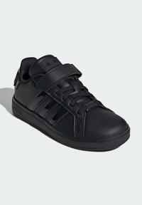 Black athletic shoes with a smooth leather upper, round toe, stitched detailing, traditional laces, and a strap across the tongue.
