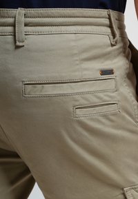 Beige cargoshorts med flera fickor, en slät yta, förstärkta sömmar och en liten märkesetikett på bakfickan.
