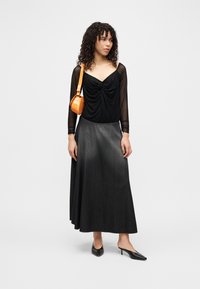 Μαύρο μπλουζάκι με μακριά μανίκια και σούρες στο λαιμό, γκρι τζιν μακρύ φόρεμα, μαύρα μυτερά παπούτσια και μικρή πορτοκαλί τσάντα ώμου.