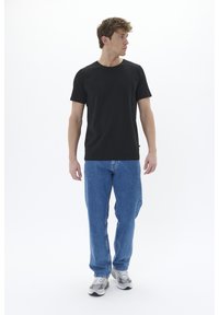 Melns īss piedurkņu T-krekls ar apaļu izgriezumu, apvienots ar zilām taisnām biksēm un pelēkiem sporta apaviem. Vienkāršs un tīrs dizains un piegriezums.