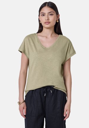 Oliven grøn, kortærmet V-hals t-shirt lavet af blødt, tekstureret stof, kombineret med løse sorte bukser og enkle smykkedetaljer.