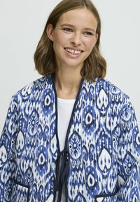 Blå och vit mönstrad kimono-liknande jacka med snörning, med stora dropp- och cirkeldesigner samt marinblå detaljer.