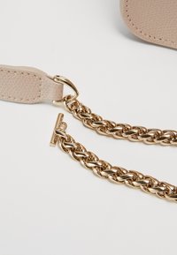 Beige textured strap attached to a thick gold chain with a toggle clasp on a white background.