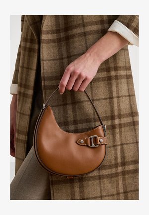 Braune Lederhandtasche mit einer geschwungenen Form, metallischen Hardware-Akzenten und einem seitlichen Tragegurt. Von einer Hand gehalten, vor einem karierten Hintergrund.