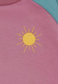 Katoenen top met een roze stof en een gele borduursel in de vorm van de zon in het midden, aangevuld met teal accenten op de schouders.