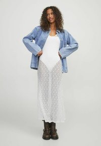 Chaqueta de mezclilla sobre un vestido largo y blanco de encaje. El vestido presenta una textura con estampado, y las botas negras hasta el tobillo completan el conjunto.