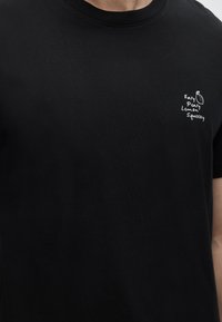 Μαύρο βαμβακερό μπλουζάκι με στρογγυλή λαιμόκοψη και μικρό λευκό γραφικό με το κείμενο «Easy Peasy Lemon Squeezy» και εικονογράφηση λεμονιού.