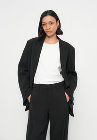 Zwarte oversized blazer met ingesneden revers, gecombineerd met een wit t-shirt en zwarte hoge taille broek. Gladde stof en een getailleerde pasvorm.