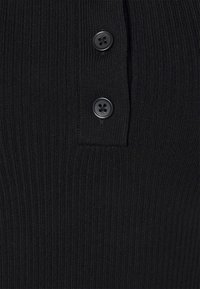 Tissu noir à côtes avec deux boutons noirs sur le plastron avant. La texture est serrée et uniforme, créant une apparence structurée.