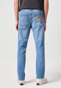 Ljusblå denimjeans med rak passform, featuring två bakfickor, sydda detaljer och en brun läderlapp på midjebandet.