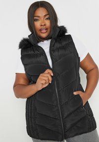 Mustapuffertakki, jossa on tekoturkistettu huppu, neljäkulmainen muotoilu, vetoketjusuljenta ja sivutaskut. Päällä valkoinen yläosa.