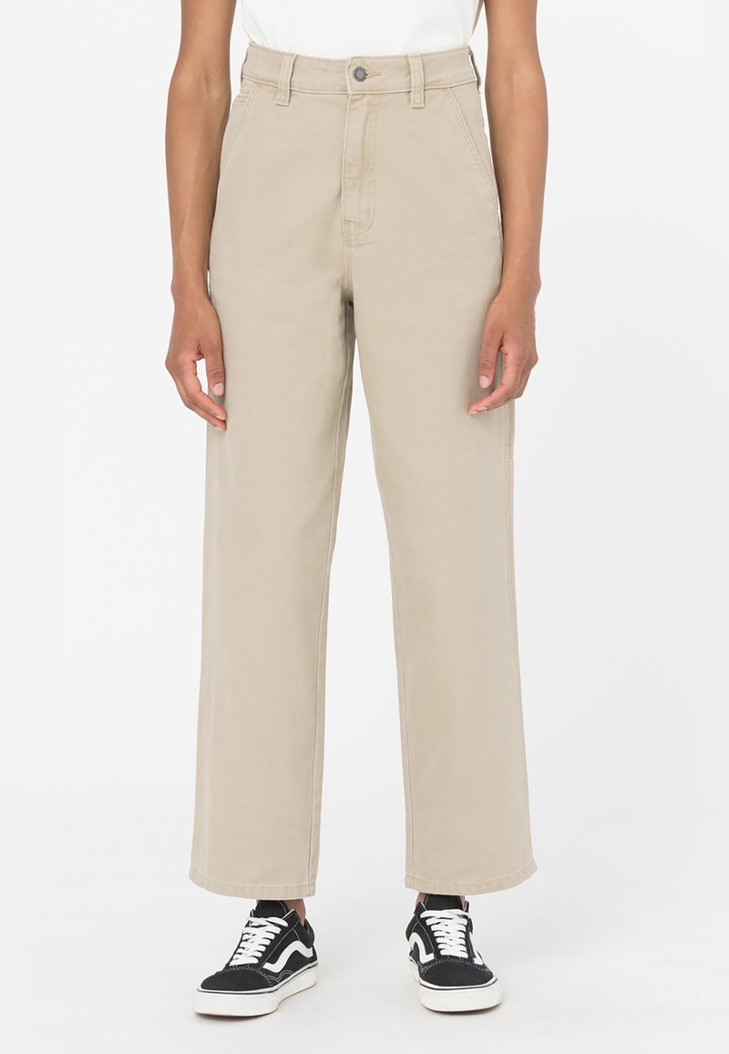 Pantaloni beige a vita alta con gamba larga, dotati di chiusura frontale a bottone e cerniera, realizzati in twill di cotone, abbinati a sneakers nere e bianche.