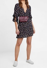 Marinblå klänning med korta volangärmar, prydd med ett blommönster i rosa och senapsgul. Matchas med en bordeauxfärgad axelremsväska och vita slip-on skor.