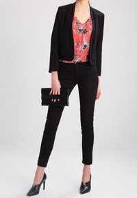 Sort blazer over en blomstermønstret rød bluse, parret med sort skinny jeans og spidse sorte hæle. Clutch-taske i hånden.