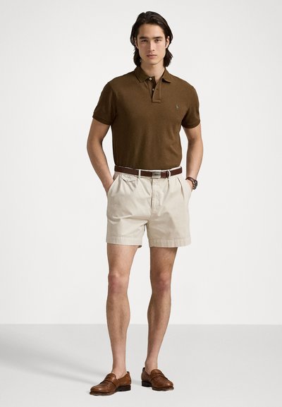 Cămașă polo maro, pantaloni scurți bej și mocasini maro. Cămașa are mâneci scurte și guler, în timp ce pantaloni scurți sunt deasupra genunchiului.