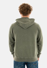 Hoodie vert olive avec une capuche à cordon, des poignets et un ourlet côtelés. Le tissu semble doux avec une texture légèrement délavée. Porté avec un jean.