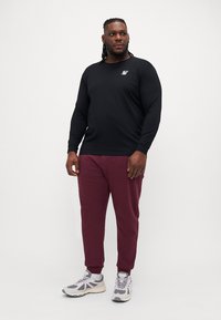 Black long-sleeve shirt with a small logo, paired with maroon joggers and gray sneakers. The outfit has a relaxed fit and casual design.