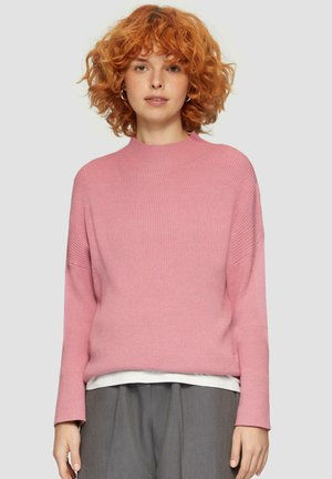 Roze geribbeld truitje met hoge hals, lange mouwen en een losse pasvorm. Gelaagd over een wit shirt en gecombineerd met grijze broek.