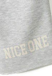 Grå bomuldsstof med en glat tekstur, der har teksten "NICE ONE" i stor, lys skrift nederst. Kanterne er let flosset.