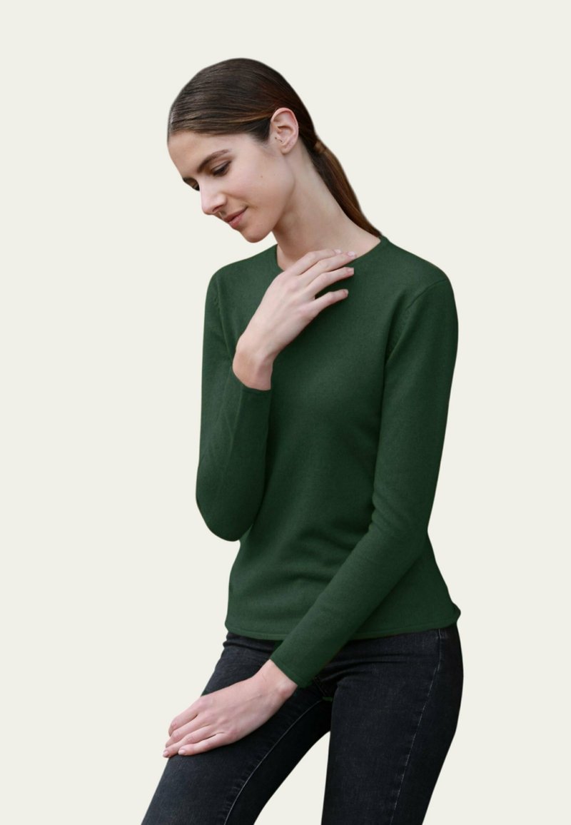 Pull à manches longues vert foncé en tricot lisse, col rond, design ajusté, associé à un jean foncé. Style relativement simple et classique.