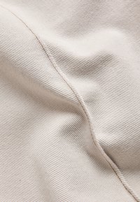 Close-up of light beige ribbed fabric with a diagonal seam and gentle folds creating texture and shadows.