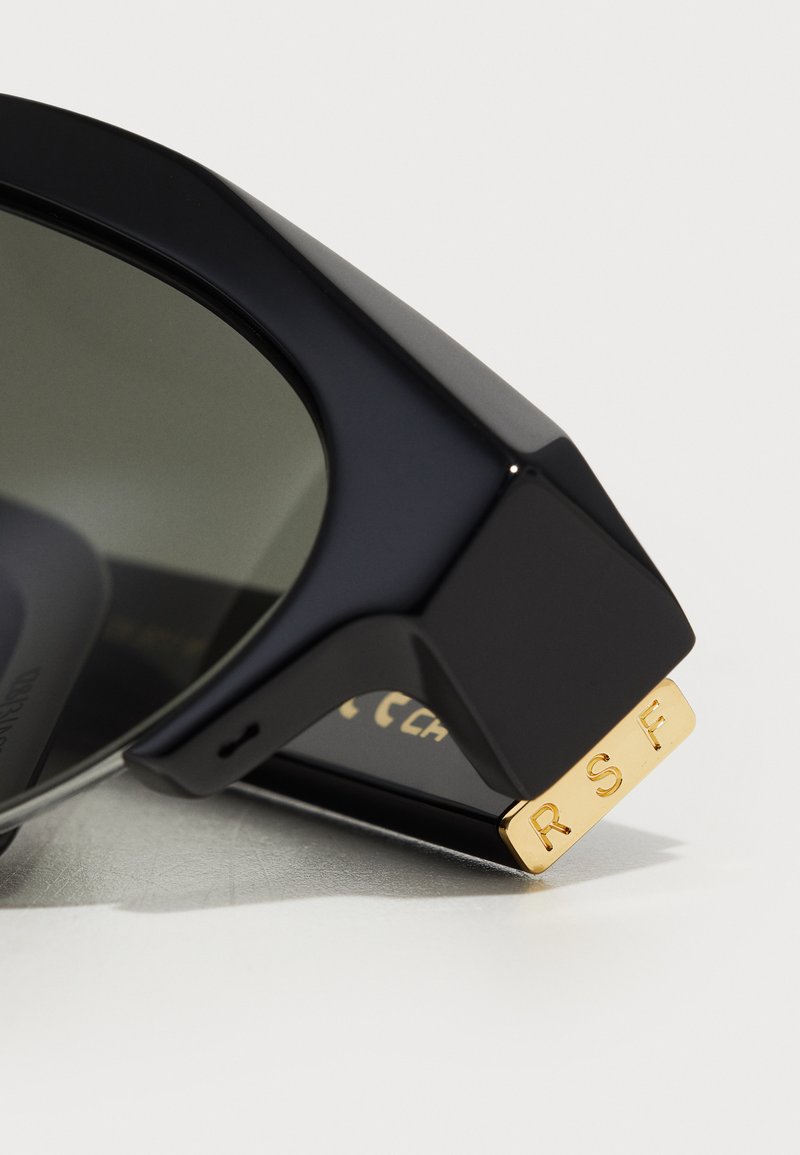 Zwarte zonnebril met donkere glazen, voorzien van een stevige, hoekige montuur. Gouden accenten met "RSF" gegraveerd aan de zijkant. Glanzende afwerking.