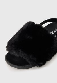 Svarta halkskyddsandaler med en mjuk, konstläderöverdela, texturerad gummisula och en minimalistisk design med ett enda brett rem.