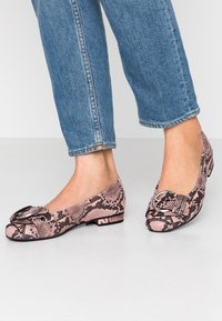 Bailarinas de piel de serpiente rosa con un acento de hebilla redonda, patrón texturizado y tacón bajo, combinadas con jeans de mezclilla arremangados.