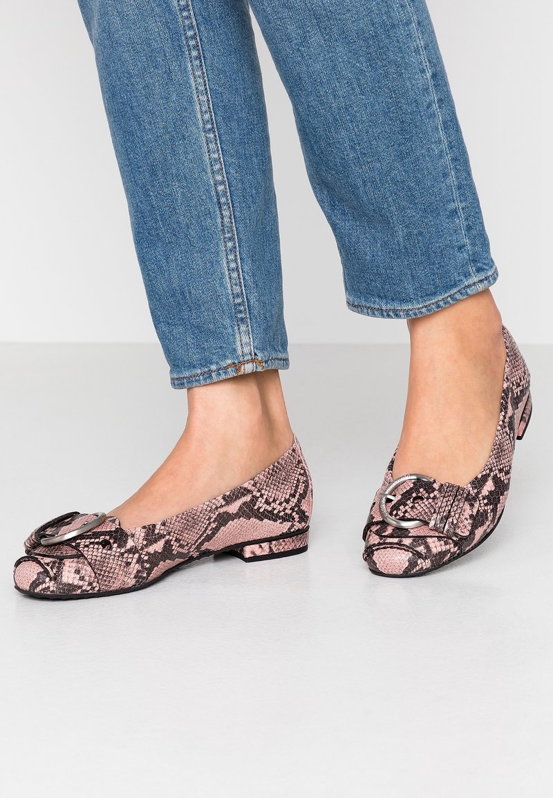 Pink snakeskin ballet flats with a round buckle accent, textured pattern, and low heel, paired with rolled-up denim jeans.