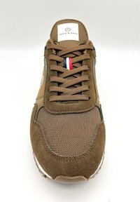 Sneaker marrone realizzato in materiali scamosciati e mesh, con punta arrotondata, design con lacci e un'etichetta con logo con accenti rossi, bianchi e blu.