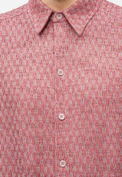 Κοντινό πλάνο ενός ροζ υφασμάτινου πουκαμίσου με κοντό κολάρο και λευκά κουμπιά στο εμπρόσθιο μέρος.