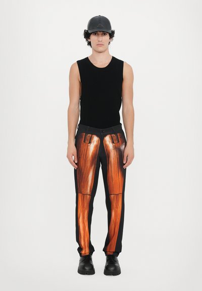 Schwarzes ärmelloses Oberteil mit glatter Textur, kombiniert mit schwarzen Hosen mit realistischem Holzmaserungsdruck und einer schwarzen Lederkappe.